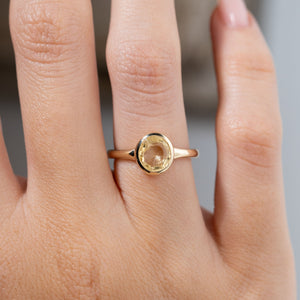 Close-up of an antique-inspired pale yellow sapphire solitaire engagement ring worn on a finger, highlighting the pale golden-yellow gemstone, polished bezel setting and slender yellow gold band.