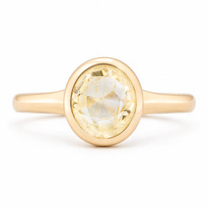 Front view of an antique-inspired pale yellow sapphire solitaire engagement ring in yellow gold, featuring an oval-cut sapphire in a smooth polished bezel setting.