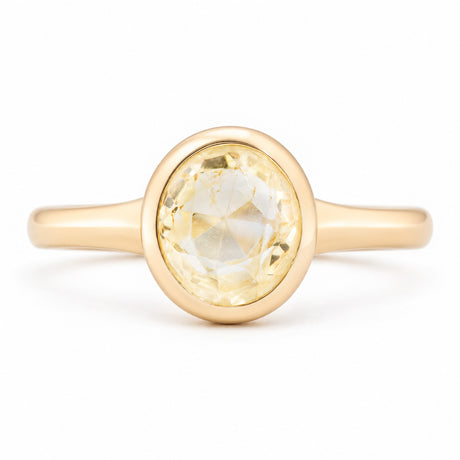 Front view of an antique-inspired pale yellow sapphire solitaire engagement ring in yellow gold, featuring an oval-cut sapphire in a smooth polished bezel setting.
