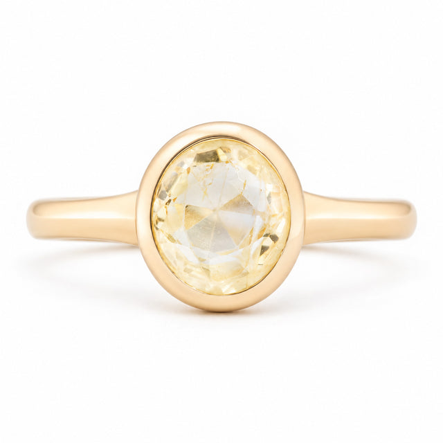 Front view of an antique-inspired pale yellow sapphire solitaire engagement ring in yellow gold, featuring an oval-cut sapphire in a smooth polished bezel setting.