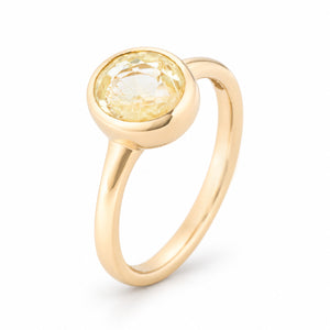 Angled studio view of an antique-inspired pale yellow sapphire solitaire engagement ring in yellow gold, showcasing its oval-cut gemstone, rounded bezel setting and elegant polished band.