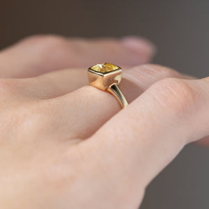 Side view of the yellow sapphire engagement ring worn on a finger, highlighting its raised bezel setting and gently tapered yellow gold band.