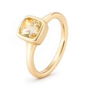 Angled studio view showcasing the golden-yellow sapphire, softly rounded square bezel and slender yellow gold band.