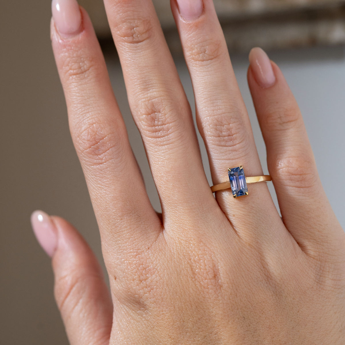 Antique-inspired blue sapphire solitaire ring worn on a hand, highlighting its elongated rectangular gemstone and minimalist yellow gold design.