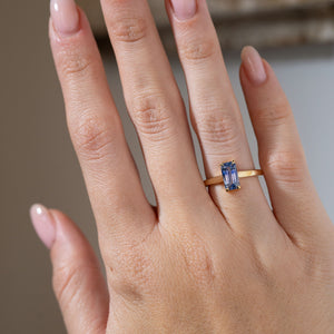 Antique-inspired blue sapphire solitaire ring worn on a hand, highlighting its elongated rectangular gemstone and minimalist yellow gold design.