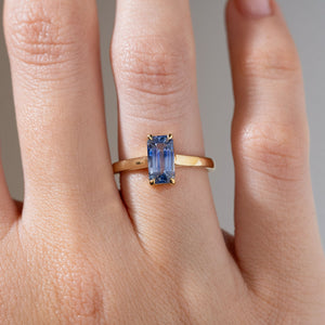 Close-up of the elongated emerald-cut sapphire ring on a finger, showcasing its striking blue facets and polished yellow gold band.