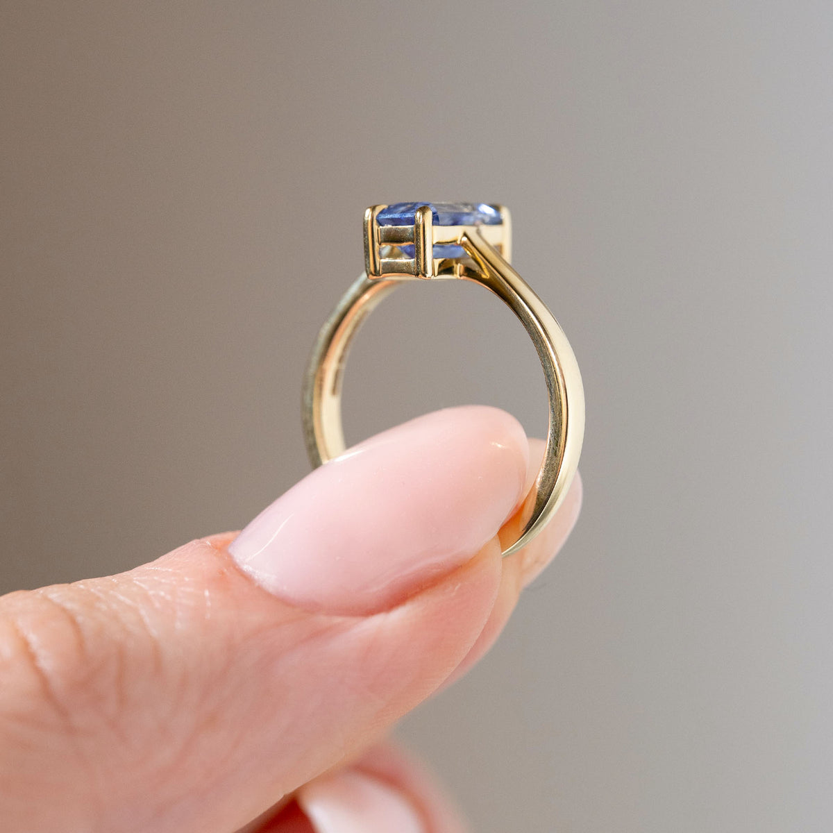 Side profile of the antique-inspired sapphire engagement ring held between fingers, showcasing the elevated gemstone setting, open gallery and polished yellow gold band.