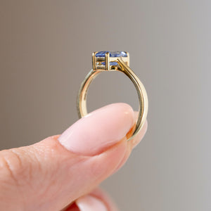 Side profile of the antique-inspired sapphire engagement ring held between fingers, showcasing the elevated gemstone setting, open gallery and polished yellow gold band.