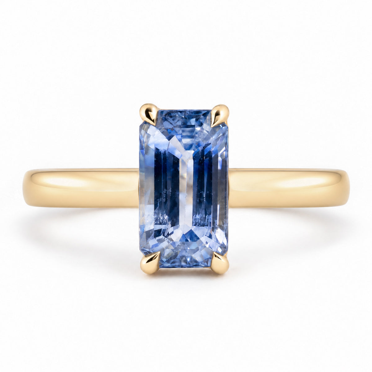 Front view of an antique-inspired blue sapphire solitaire engagement ring, featuring an elongated emerald-cut gemstone in a polished yellow gold claw setting.