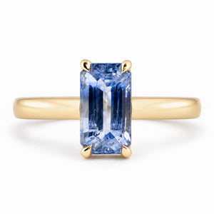 Front view of an antique-inspired blue sapphire solitaire engagement ring, featuring an elongated emerald-cut gemstone in a polished yellow gold claw setting.