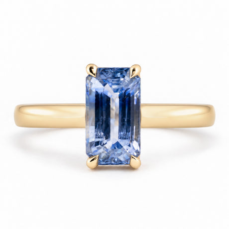 Front view of an antique-inspired blue sapphire solitaire engagement ring, featuring an elongated emerald-cut gemstone in a polished yellow gold claw setting.