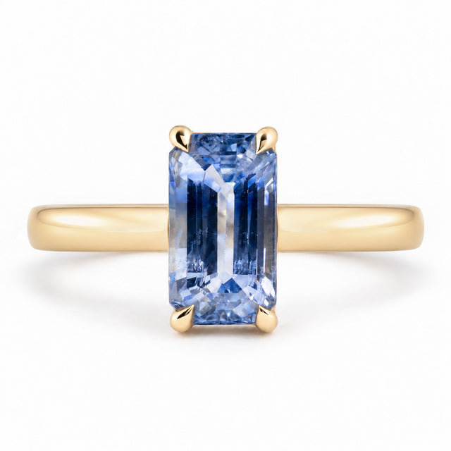 Front view of an antique-inspired blue sapphire solitaire engagement ring, featuring an elongated emerald-cut gemstone in a polished yellow gold claw setting.