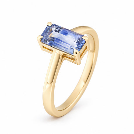Angled studio view showcasing the step-cut blue sapphire, four gold claws and elegant tapered band.