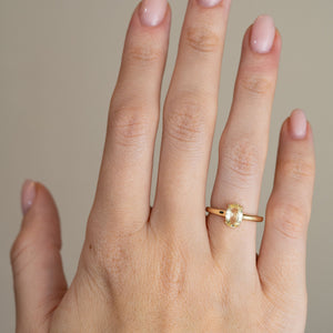 A delicate oval sapphire engagement ring worn on a hand, highlighting its subtle champagne-yellow tones and slender gold band.