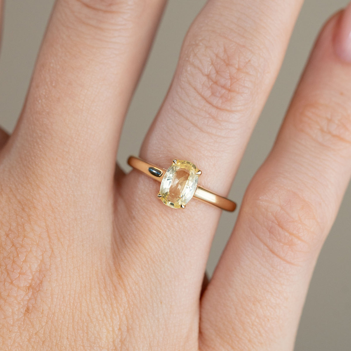 Close-up of the antique-inspired yellow gold ring on a finger, showing the elongated oval sapphire and refined claw setting.