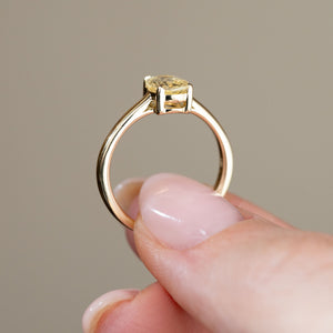 Rear profile of the antique-style solitaire ring held between fingers, showcasing the open gallery beneath the sapphire and slim yellow gold shank.