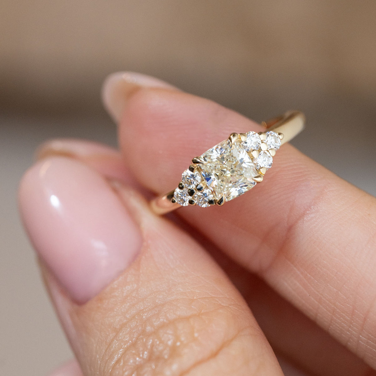 Hand-held close-up of the cushion-cut centre diamond with decorative brilliant-cut diamond clusters on either side.