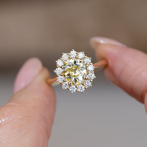Hand-held close-up of the pale yellow old-mine cut diamond framed by sparkling white diamonds in a classic cluster design.