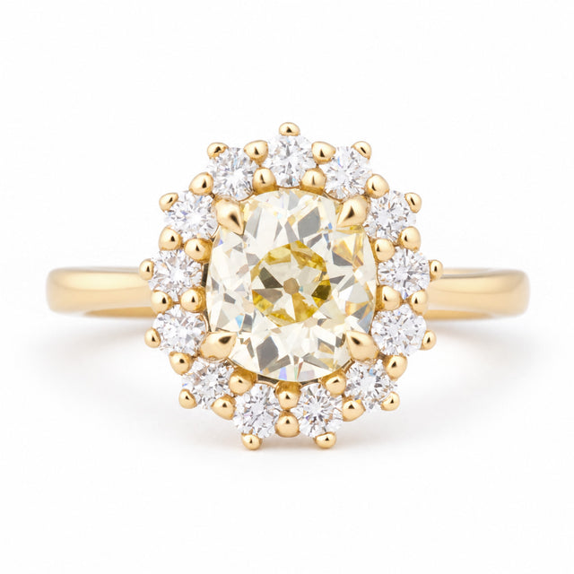 Antique-inspired yellow cushion old-mine cut diamond cluster engagement ring in yellow gold, surrounded by a halo of brilliant-cut white diamonds.