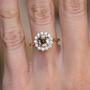 Brown diamond cluster engagement ring worn on a finger, showcasing the contrasting white diamond halo and yellow gold band.