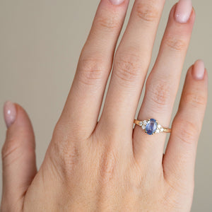 Blue sapphire and diamond cluster engagement ring worn on a hand, showing its elegant proportions and slim yellow gold band.