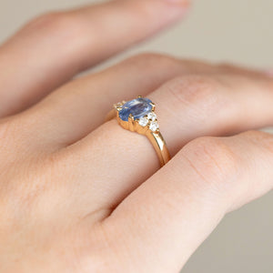 Side-angled photograph of the sapphire and diamond engagement ring worn on a hand, revealing its raised setting and gold band.