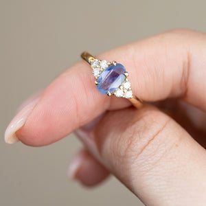 Detailed close-up of a blue sapphire ring held between fingers, highlighting the oval gemstone, gold claws and symmetrical diamond clusters.