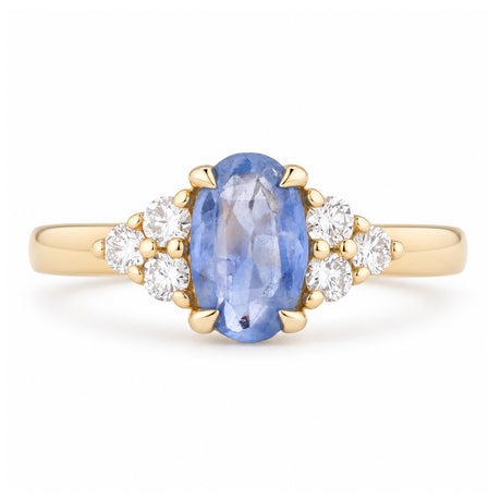 Vintage-inspired blue sapphire and diamond trefoil engagement ring in yellow gold, featuring an oval blue sapphire flanked by sparkling diamond clusters.