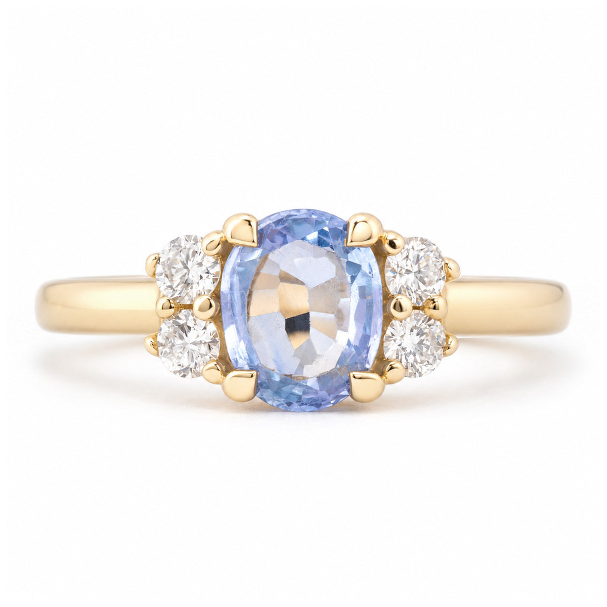 Front view of a vintage-inspired blue sapphire and diamond cluster engagement ring in yellow gold, featuring an oval-cut pale blue sapphire flanked by four sparkling round diamonds.
