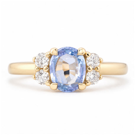 Front view of a vintage-inspired blue sapphire and diamond cluster engagement ring in yellow gold, featuring an oval-cut pale blue sapphire flanked by four sparkling round diamonds.