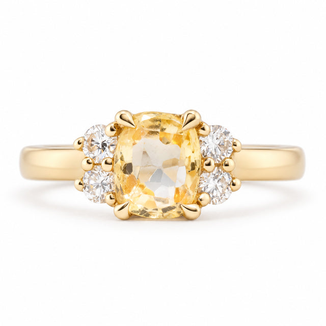 Front view of a vintage-inspired yellow sapphire and diamond cluster engagement ring in yellow gold, featuring a cushion-cut yellow sapphire flanked by four sparkling round diamonds.