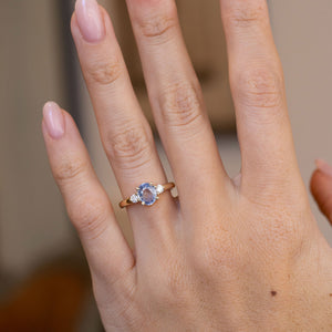 Blue sapphire three-stone engagement ring worn on a hand, showcasing its delicate proportions and classic design.