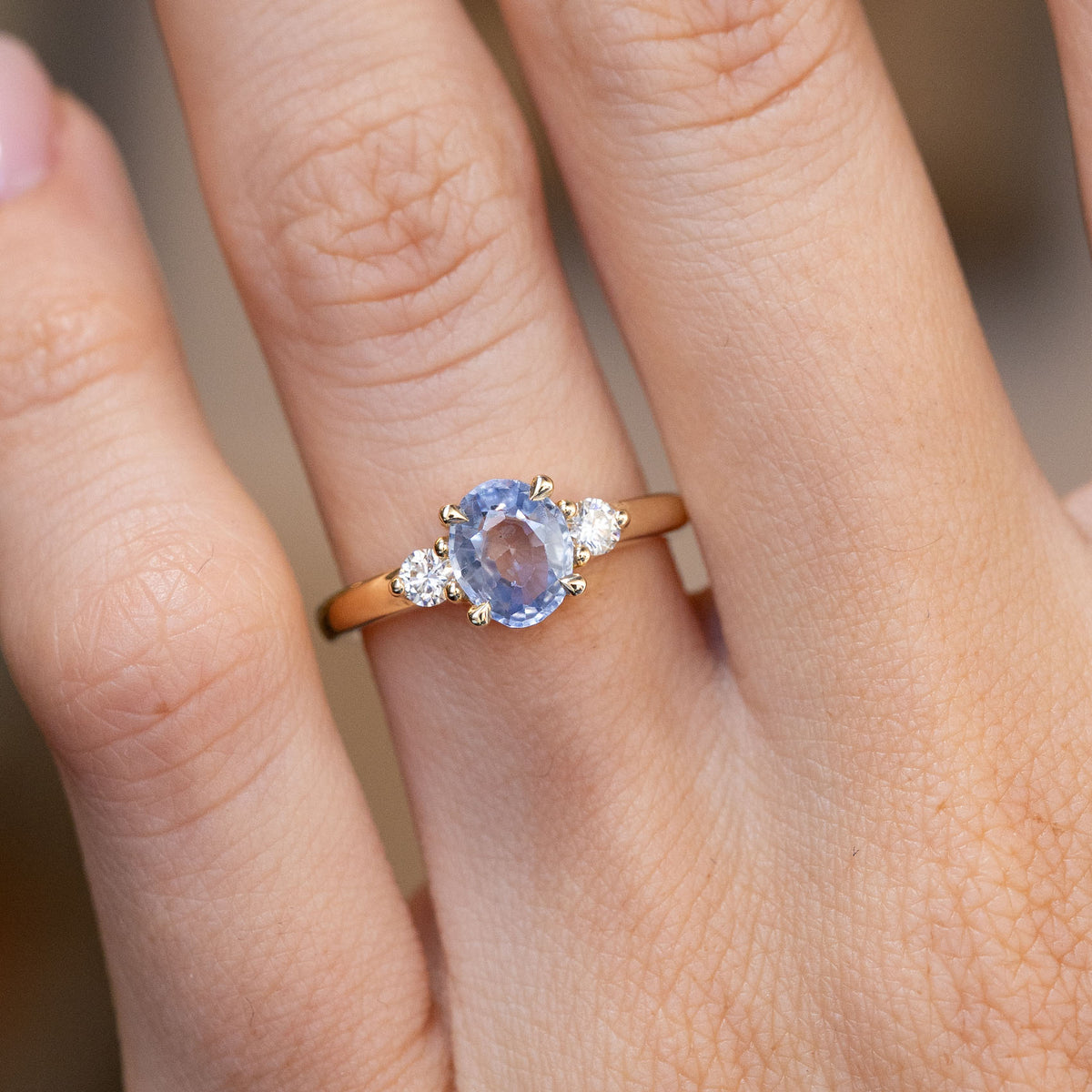 Close-up of the oval blue sapphire flanked by two brilliant-cut white diamonds, worn on a finger.