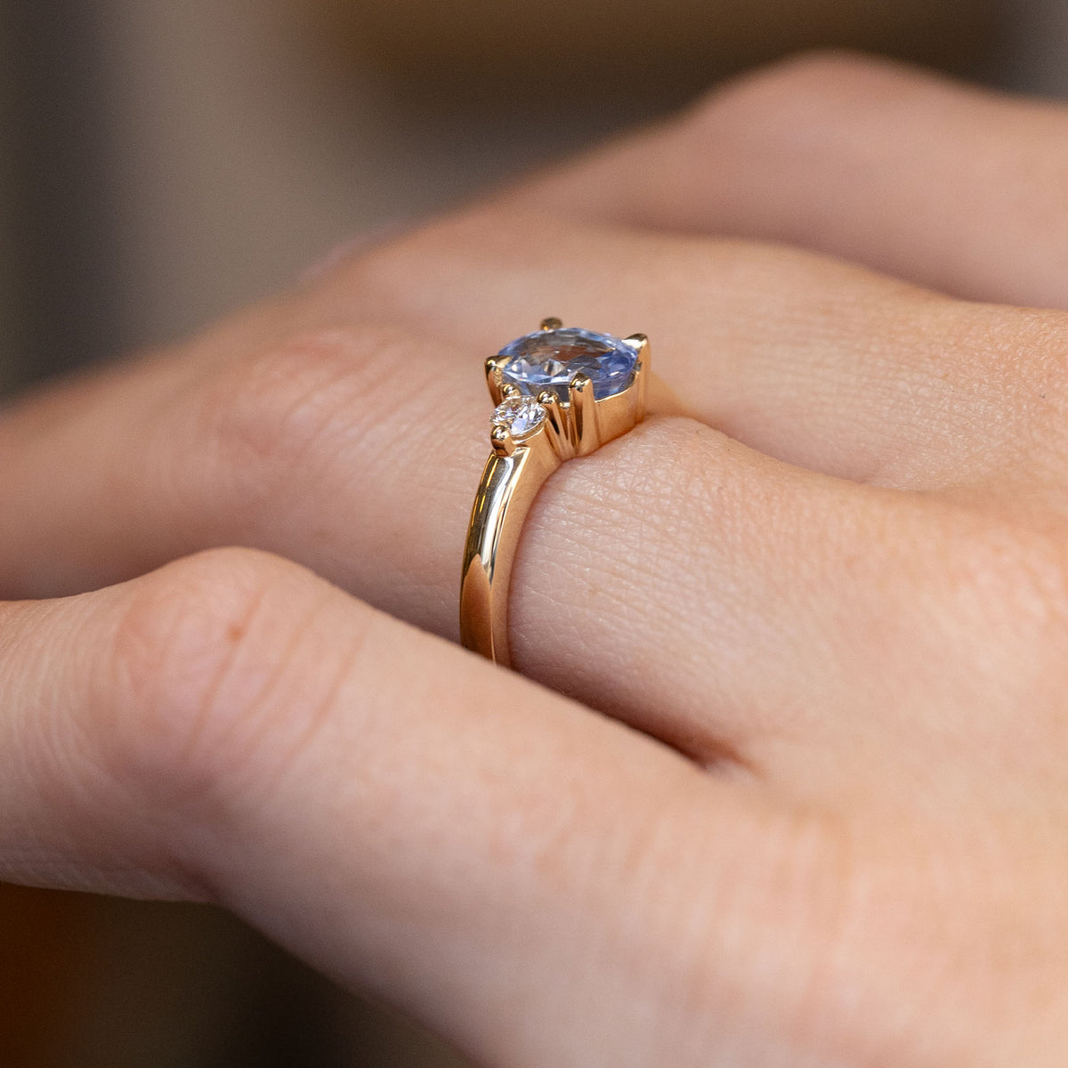Side-angle view of the sapphire and diamond ring worn on a hand, highlighting the raised setting and delicate gold detailing.