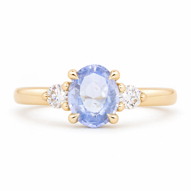 Antique-inspired blue oval sapphire and diamond three-stone engagement ring in yellow gold, featuring two round brilliant-cut diamond shoulders.