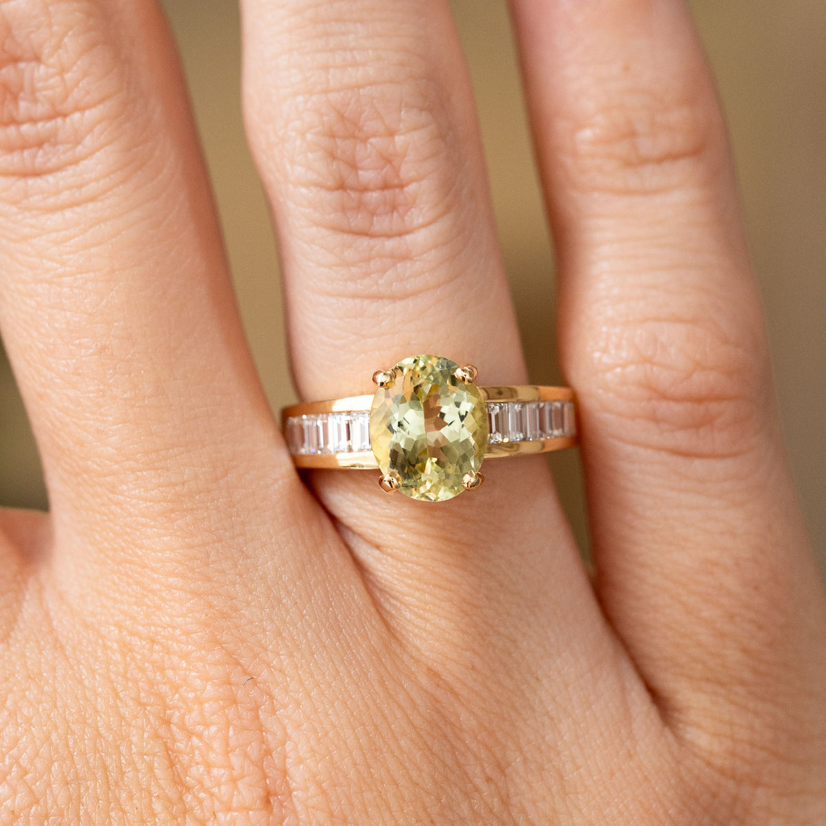 Close-up of a vintage 18ct yellow gold engagement ring featuring an oval green beryl flanked by ten channel-set baguette diamonds.