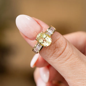 Vintage oval-cut green beryl and diamond ring held between the fingers, with five channel-set baguette diamonds on each shoulder.
