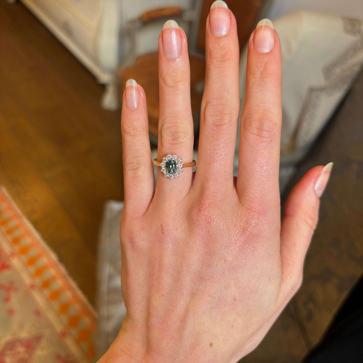 Green sapphire and diamond cluster engagement ring worn on ring finger of left hand.