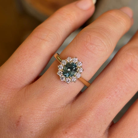 Green sapphire and diamond cluster engagement ring worn on hand closeup