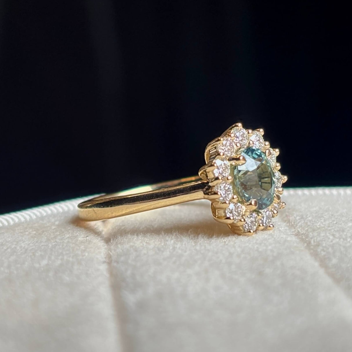 Green sapphire and diamond cluster yellow gold engagement ring on light background. 