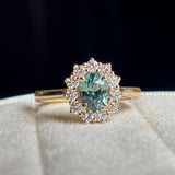 Green sapphire and diamond cluster engagement ring worn with wedding band to show scale. 