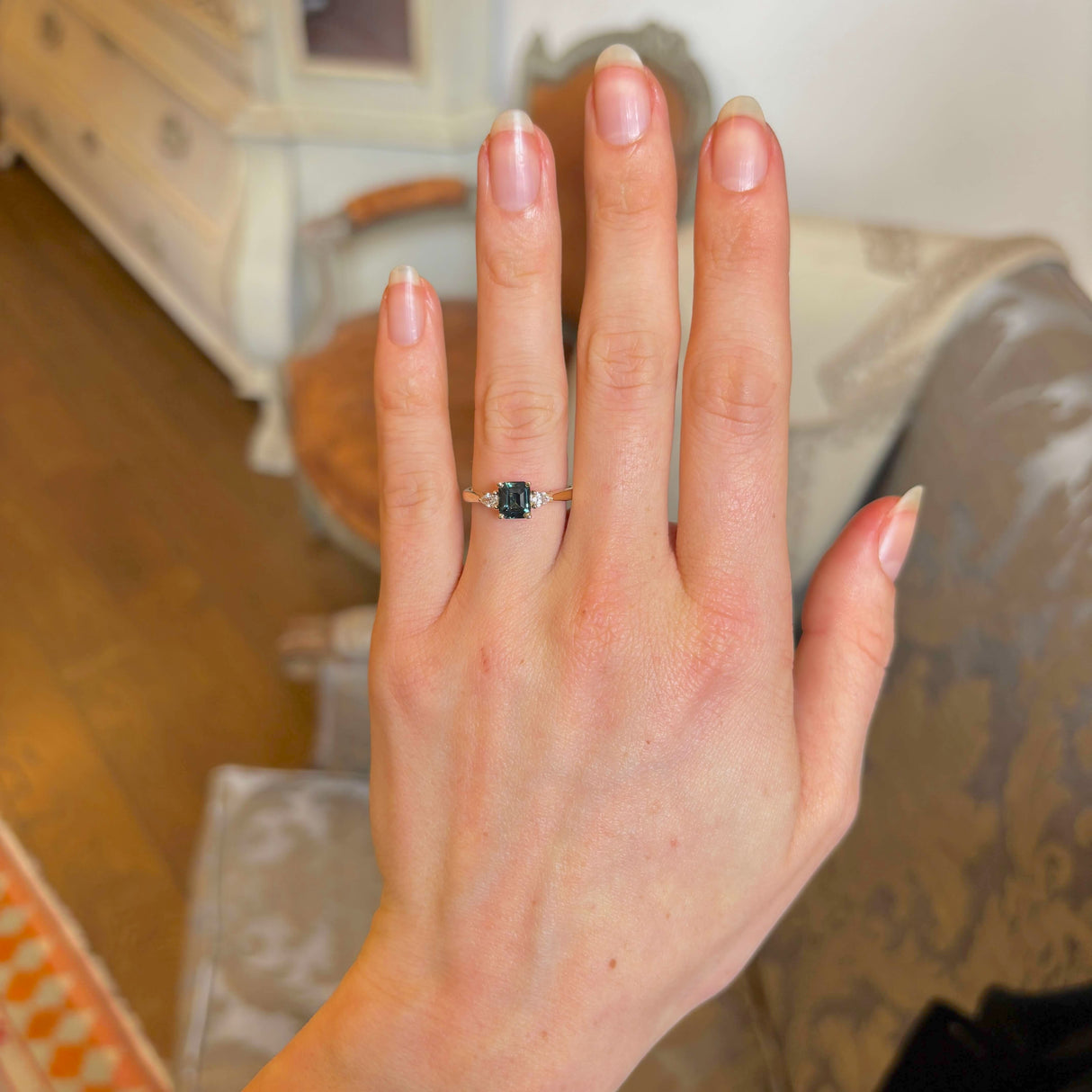 Green sapphire and diamond three-stone engagement ring on hand showing scale