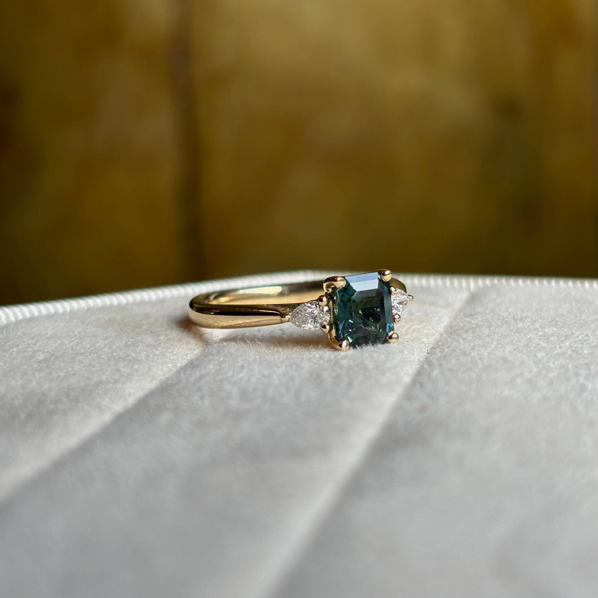 Green sapphire and diamond three-stone engagement ring angled to show pear-cut diamonds and band. 
