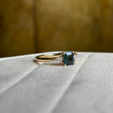 Green sapphire and diamond three-stone engagement ring angled to show pear-cut diamonds and band. 