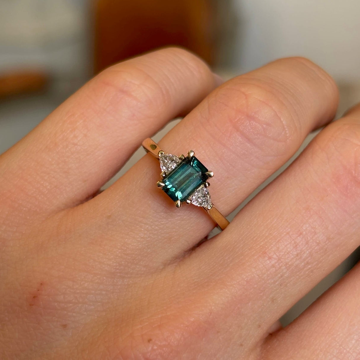 Green sapphire and diamond three-stone engagement ring on hand up close