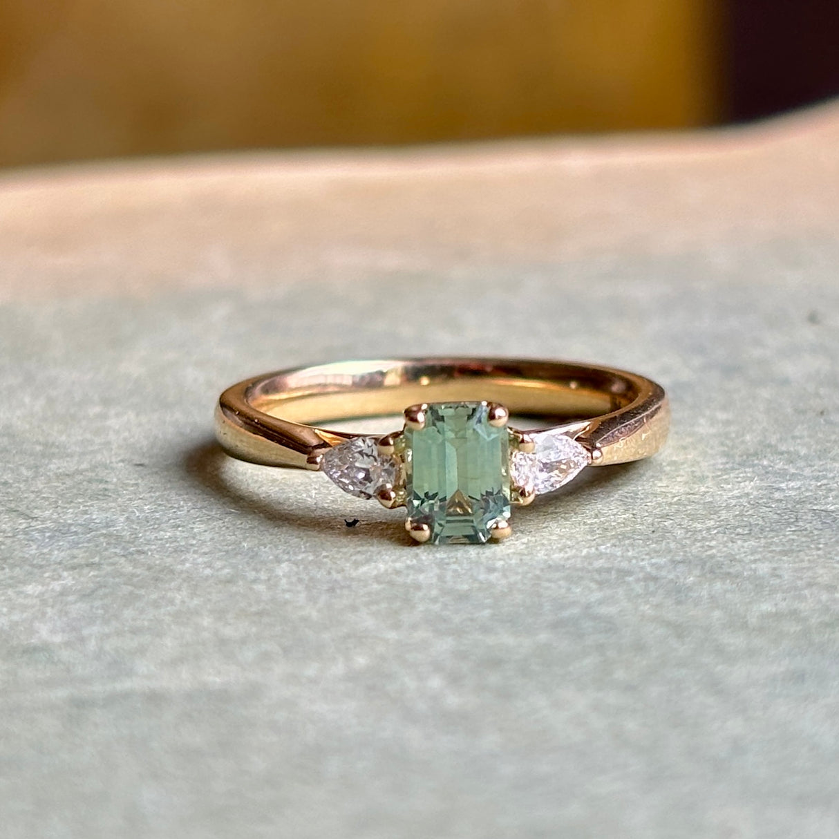 Green sapphire and diamond three-stone engagement ring displayed on a neutral background, emphasising craftsmanship and gemstone proportions.
