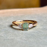 Green sapphire and diamond three-stone engagement ring displayed on a neutral background, emphasising craftsmanship and gemstone proportions.