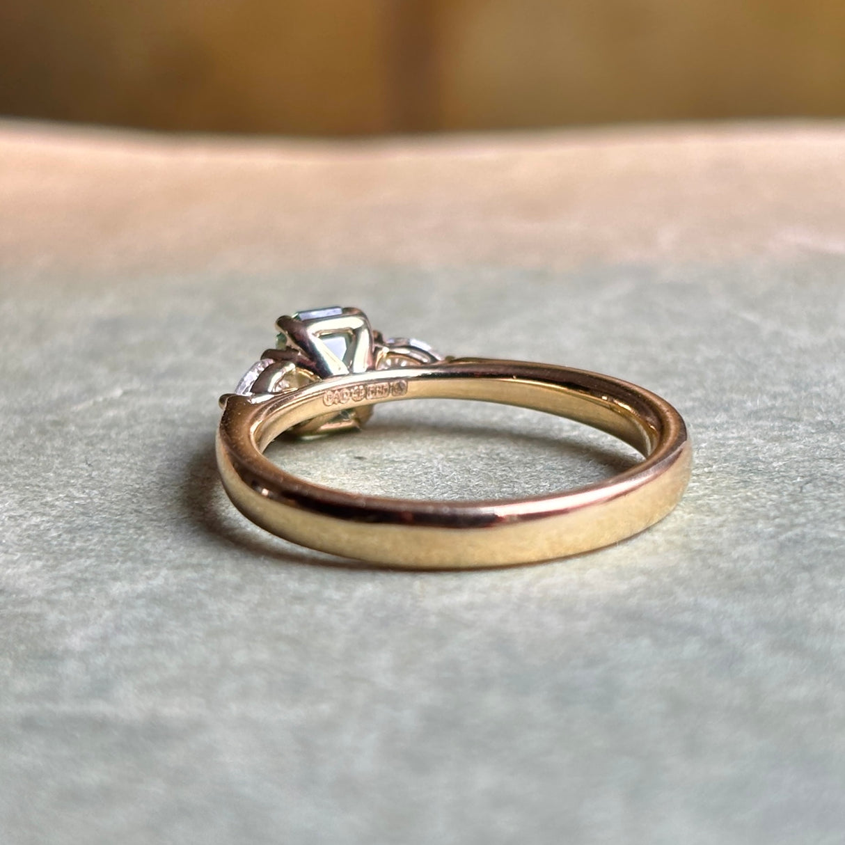 Green sapphire and diamond three-stone engagement ring showing the setting structure, hallmarks and band detail in yellow gold.
