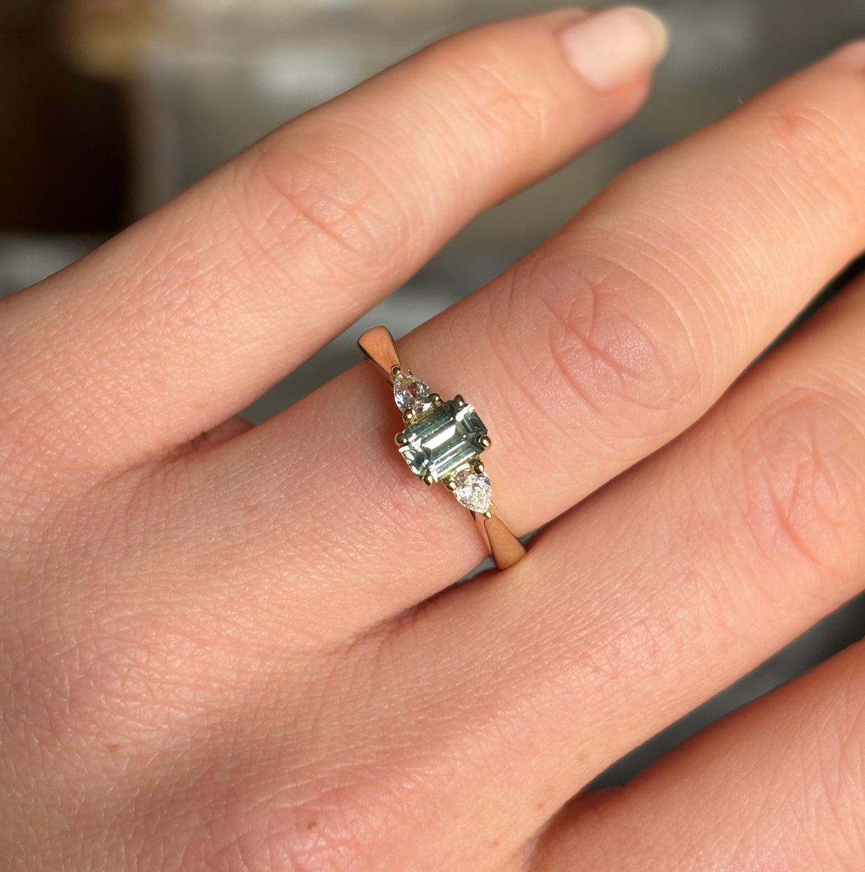 Green sapphire and diamond three-stone engagement ring worn on the engagement ring finger, highlighting colour and everyday wearability.