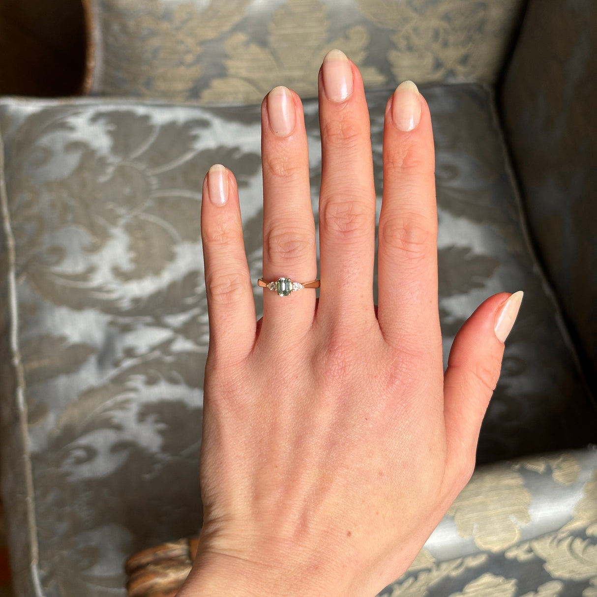 Green sapphire and diamond three-stone engagement ring worn on the hand, providing scale and overall appearance when worn.